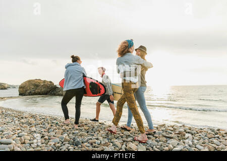 Happy amici con tavole da surf a piedi sulla spiaggia sassosa Foto Stock