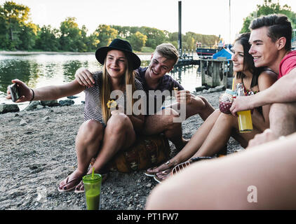 Gruppo di amici seduti insieme a un barbecue e prendendo un selfie al Riverside Foto Stock