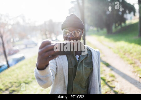 Giovane uomo in piedi nel parco, tenendo selfie dello smartphone Foto Stock