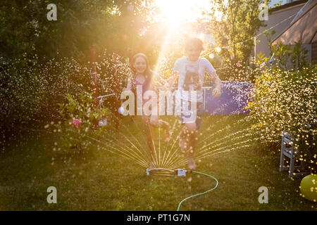 Fratello e Sorella e divertirsi con sprinkler prato in giardino Foto Stock