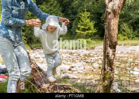 Madre tenendo le mani della figlia, bilanciamento sul tronco di albero Foto Stock