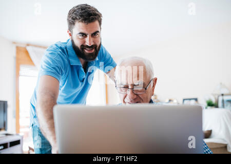 Nipote di adulti insegnamento a suo nonno per uso portatile Foto Stock