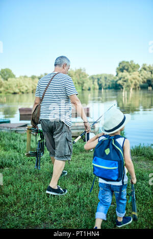 Vista posteriore del nonno e nipotino con sedia di pesca e canne da pesca Foto Stock