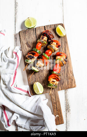 Grill con gli spiedini di pollo alla griglia, pomodoro, peperoni e zucchine sul tagliere Foto Stock