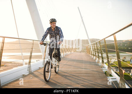 Giovane uomo Bicicletta Equitazione su un ponte al tramonto Foto Stock