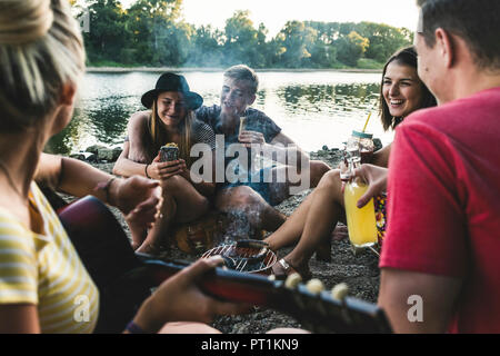 Gruppo di amici seduti insieme a un barbecue al Riverside Foto Stock