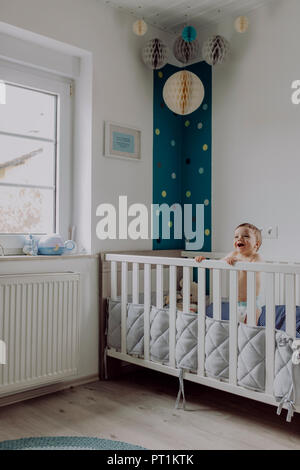 Baby boy in piedi nella sua culla, ridendo Foto Stock