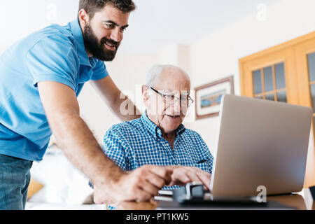 Nipote di adulti insegnamento a suo nonno per uso portatile Foto Stock