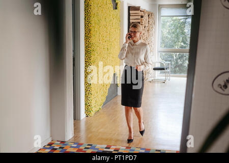 Imprenditrice sorridente sul cellulare sul pavimento per ufficio Foto Stock