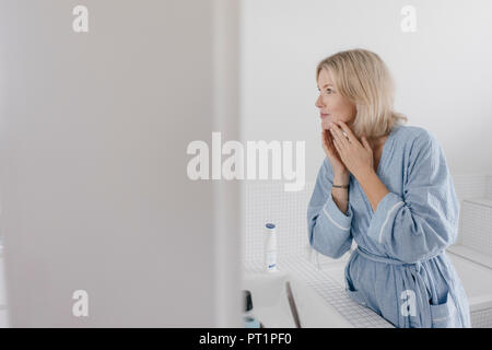 Donna matura guardando nello specchio del bagno Foto Stock