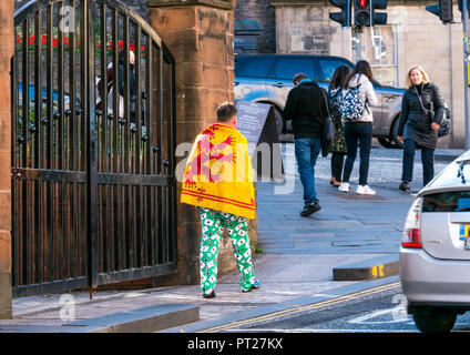 Holyrood, Edimburgo, Scozia, Regno Unito, 6 ottobre 2018. Tutti sotto uno striscione (AUOB) Scottish marzo Rally e per l'indipendenza. AOUB è un pro-indipendenza campagna per il cui obiettivo principale è quello di marzo ad intervalli regolari fino a quando non raggiunge la Scozia indipendenza. Un uomo cammina su una strada che indossa una carta da gioco tuta con un scozzese leone rampante bandiera drappeggiato sopra le spalle Foto Stock