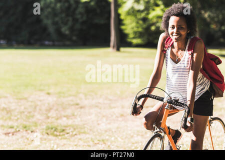 Ritratto di sorridente giovane donna in bicicletta nel parco Foto Stock