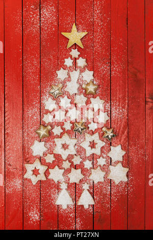 Biscotti di Natale e a forma di stella di Natale formando baubles albero di Natale sul rosso sfondo di legno Foto Stock