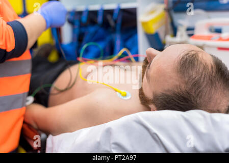 Medico di emergenza le mani, fissaggio elettrodi ECG sul torace del paziente in ambulanza Foto Stock