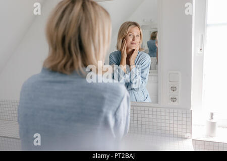 Donna matura guardando nello specchio del bagno Foto Stock