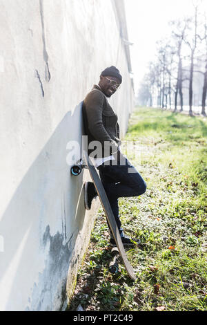 Cool giovane uomo pendente con lo skateboard sulla parete in città Foto Stock