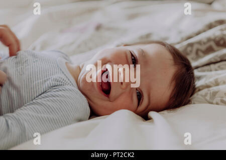 Happy baby, giacente sul letto, ridendo Foto Stock