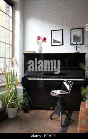 Il pianoforte con il computer portatile su uno sgabello in confortevole appartamento loft Foto Stock