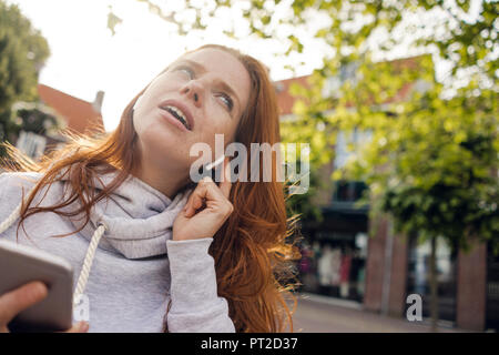 Redheaded donna utilizzando gli auricolari dello smartphone e Foto Stock