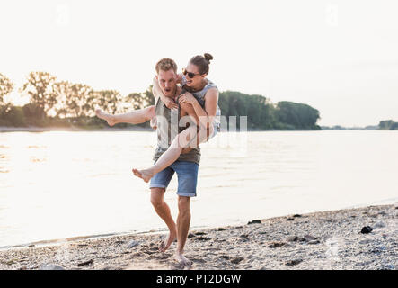 Giovane uomo dando ragazza piggyback ride presso la riva del fiume Foto Stock