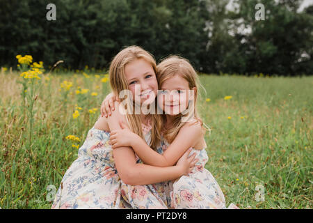 Due piccole sorelle che abbraccia ogni altra su un prato Foto Stock