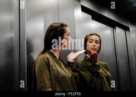 Giovane donna guardando in uno specchio in ascensore soffia un bacio Foto Stock