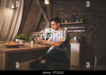 Giovane uomo utilizzando tablet in cucina a casa Foto Stock