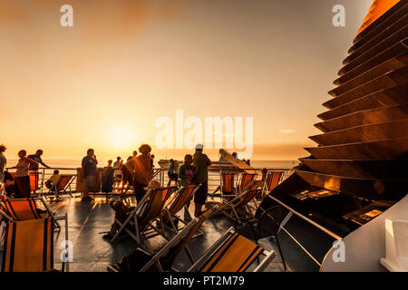 I passeggeri sul ponte di una nave con una vista del sole serale Foto Stock