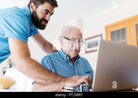 Nipote di adulti insegnamento a suo nonno per uso portatile Foto Stock