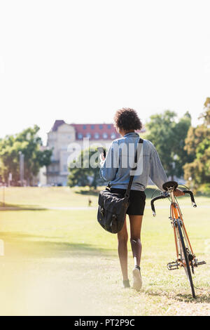 Giovane donna con un telefono cellulare per bicicletta di spinta in posizione di parcheggio Foto Stock