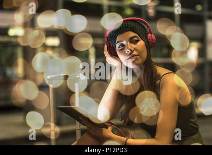 Ritratto di giovane donna con le cuffie e tablet in attesa nella stazione di notte Foto Stock