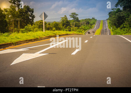 Autostrada di pendenza con sole e verde isola di traffico. Quattro corsie con traffico verde isola. Il Provinciale immenso road passando attraverso un verde Foto Stock