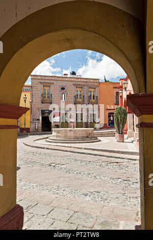 Vista attraverso un'arcata del Bernal fontana pubblica a Saragozza e Hidalgo strade nel bellissimo villaggio coloniale di Bernal, Queretaro, Messico. Bernal è una pittoresca città coloniale noto per la Peña de Bernal, un monolito gigante che domina il piccolo borgo è la terza più alta del pianeta. Foto Stock