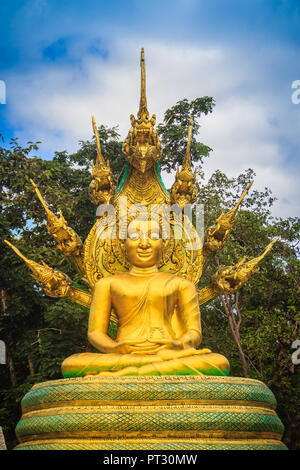 Beautiful golden statua del Buddha con sette Phaya Naga capi sotto nuvole bianche e blu sullo sfondo del cielo. Outdoor golden Buddha seduto immagine protetta da Foto Stock