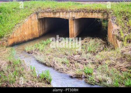 Cemento armato tombini scatolari sotto la strada asfaltata. Box canale sotterraneo è una struttura che consente il flusso di acqua sotto una strada, ferrovia, sentiero o simila Foto Stock