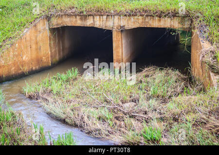 Cemento armato tombini scatolari sotto la strada asfaltata. Box canale sotterraneo è una struttura che consente il flusso di acqua sotto una strada, ferrovia, sentiero o simila Foto Stock