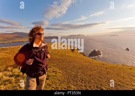 Uomo in piedi sulle scogliere con le isole sullo sfondo illuminato da dietro, la penisola di Dingle, Irlanda Foto Stock