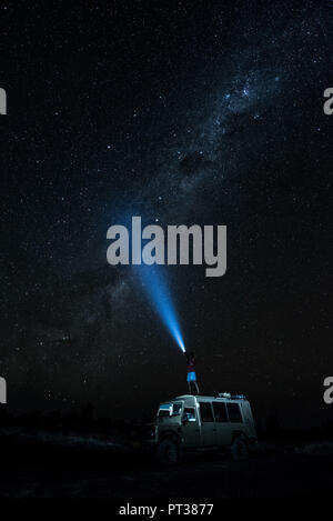 Uomo in piedi su una jeep e splendente di una torcia elettrica nel cielo stellato, creative lunga esposizione, Namibia, Africa Foto Stock