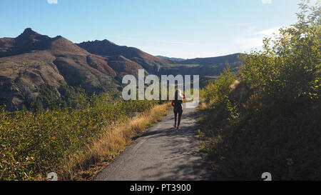 Donna in felpa rossa passeggiate il sentiero di confine a Johnston Ridge Osservatorio sul Monte Saint Helens su un chiaro e limpido giorno. Foto Stock