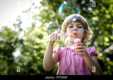 Ragazza bionda in abito rosa soffiando bolle di sapone Foto Stock