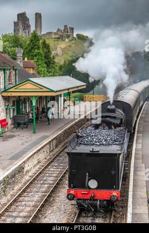 Come minaccia aria di tempesta sopra il castello, una locomotiva a vapore tira nella pittoresca stazione presso Corfe nel Dorset. Foto Stock