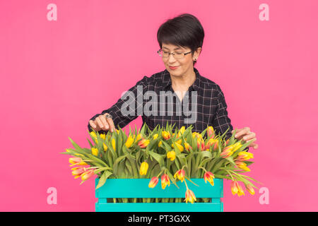 Floristics, vacanze e concetto di persone - donna di mezza età della scatola di contenimento di tulipani su uno sfondo rosa Foto Stock