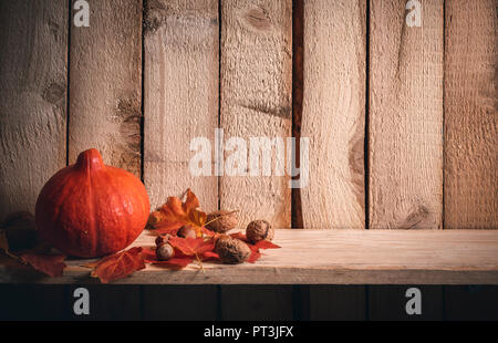 Autunno del telaio con un arancione zucca circondato da foglie rosse, noci e nocciole, su un ripiano contro un annata sullo sfondo di legno. Foto Stock