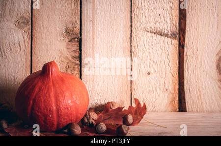 Autunno banner rustico con un arancione zucca su foglie rosse, circondato da noci e nocciole, su un annata sullo sfondo di legno. Foto Stock