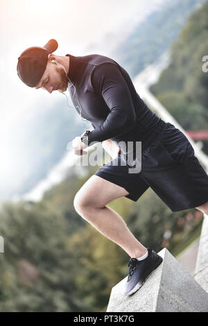 Muscolare atleta barbuto controllo calorie bruciate su smart guarda dopo una buona sessione di allenamento sul parco della città. Foto Stock