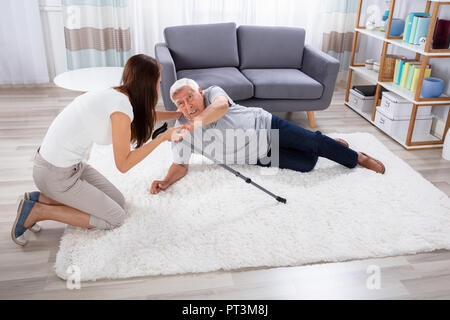 Donna aiutando il padre dopo la caduta su un tappeto a casa Foto Stock