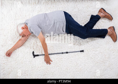 Inconscio Senior Uomo con bastone giacente su un tappeto a casa Foto Stock