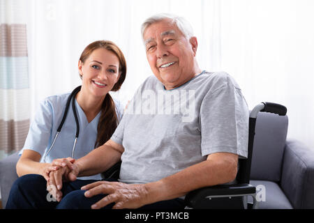 Ritratto di un sorridente Senior uomo seduto su una sedia a rotelle con infermiera femmina Foto Stock
