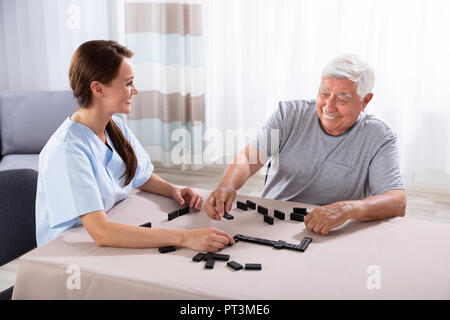 Giovani femmine custode guardando l'uomo anziano GIOCA Domino su scrivania Foto Stock