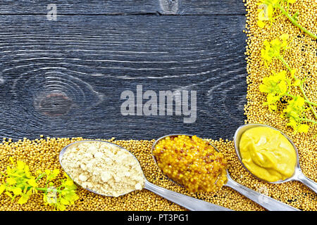 Telaio di semi e fiori di senape, senape e salsa di granulare, polvere in cucchiai sullo sfondo di un nero pannello di legno Foto Stock